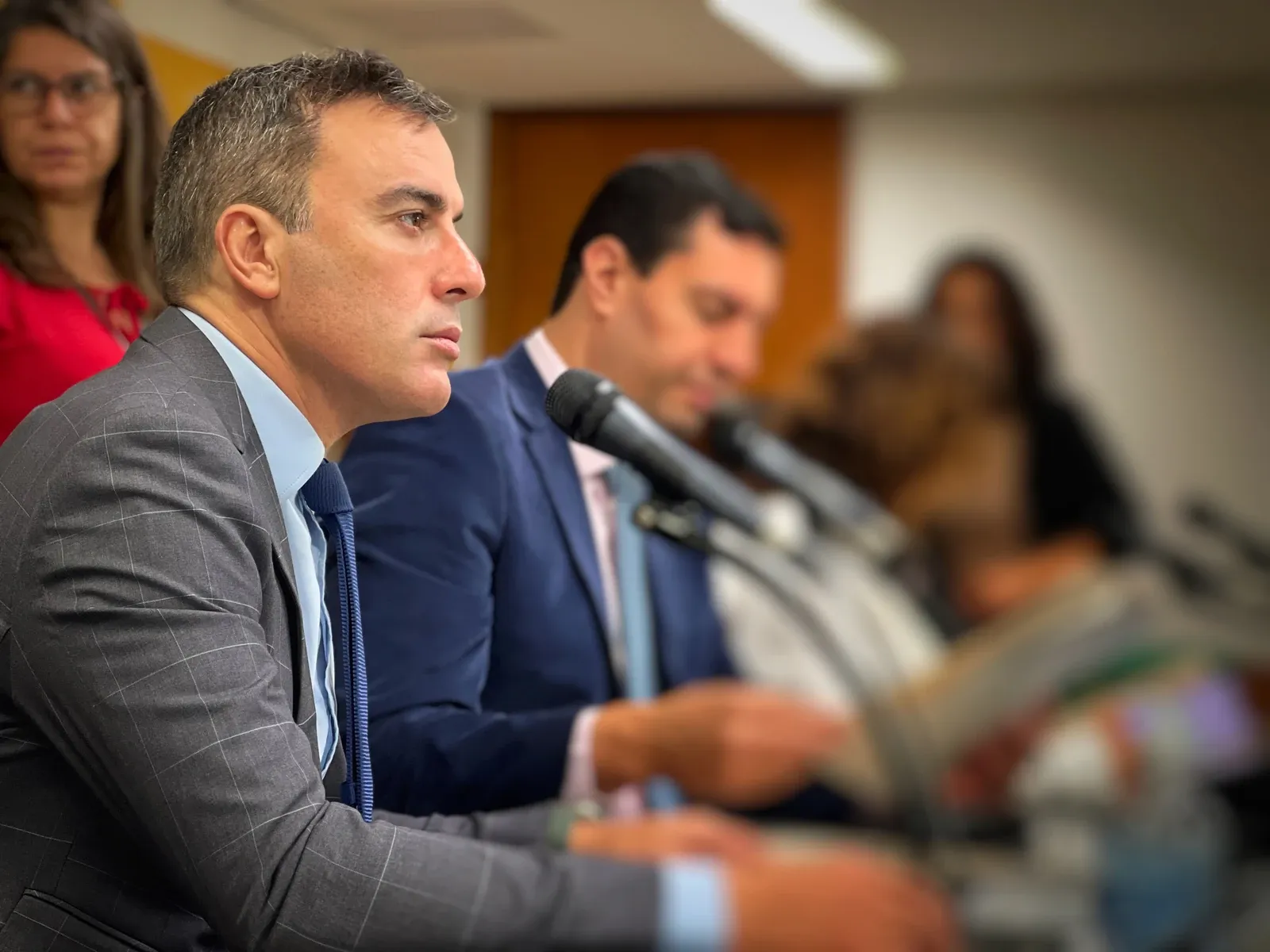 Noraldino Jr. de perfil, concentrado, ao microfone em reunião de trabalho